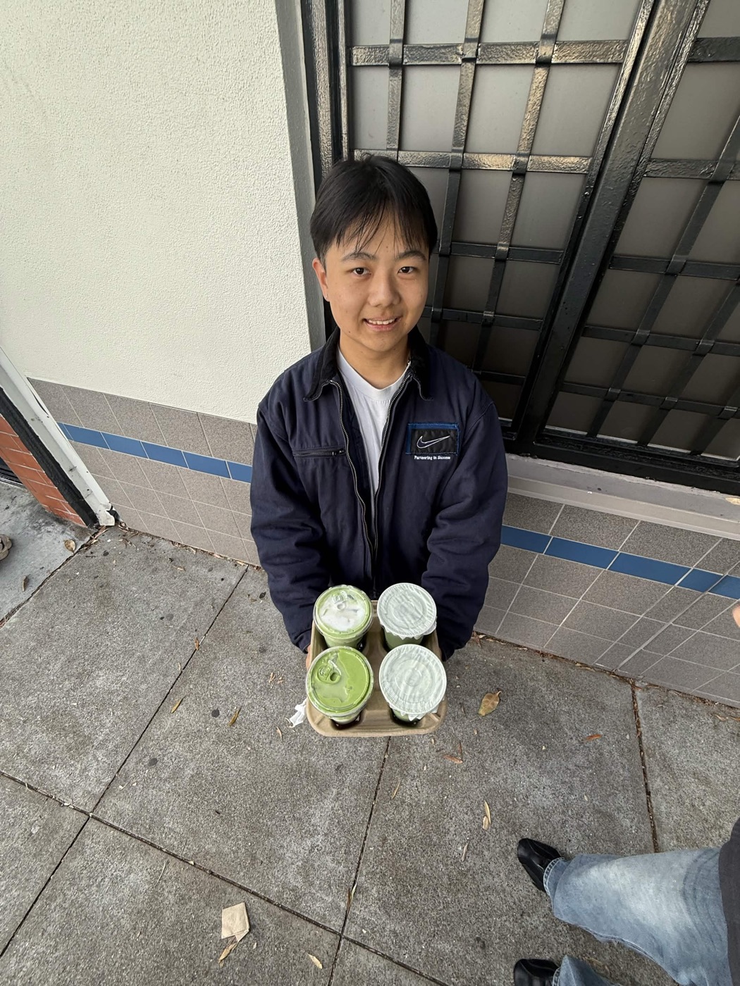 Morris holding a tray of four matcha drinks on the sidewalk
