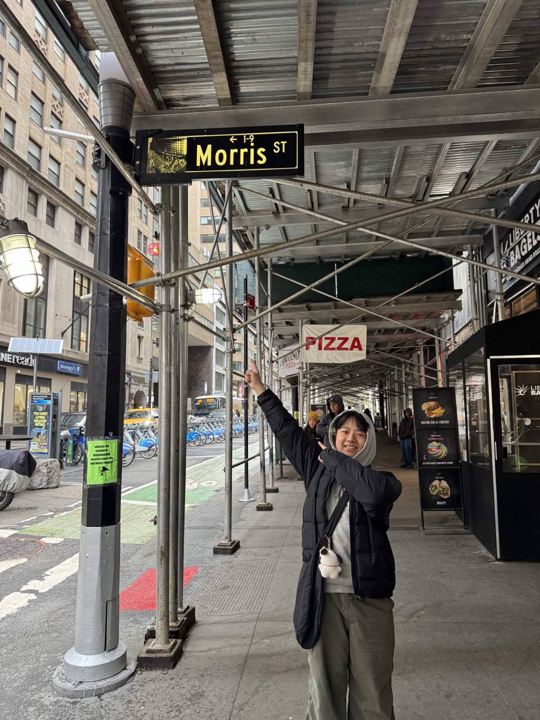 Morris pointing up at a Morris St street sign under scaffolding